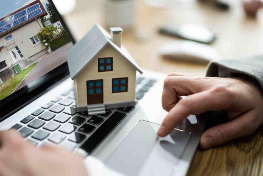 Laptop with a house model, screen showing a solar-paneled house, representing online property search.